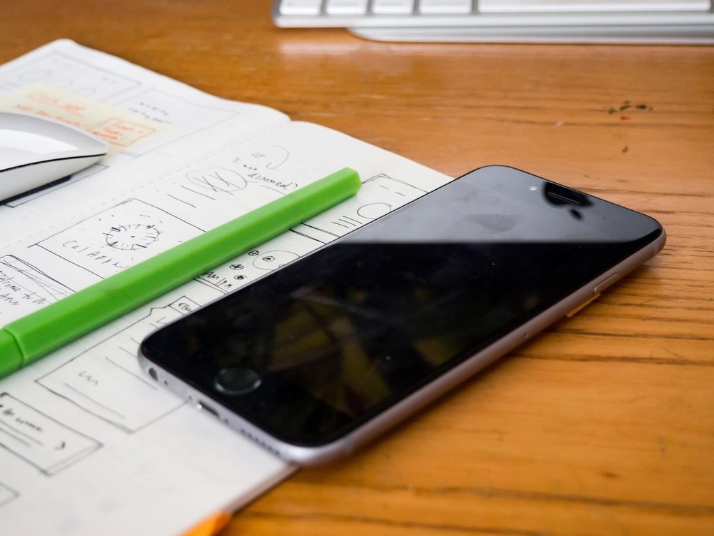 A phone beside interface wireframes on a desk