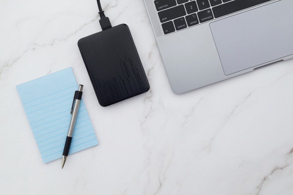 A portable drive and notebook beside a laptop